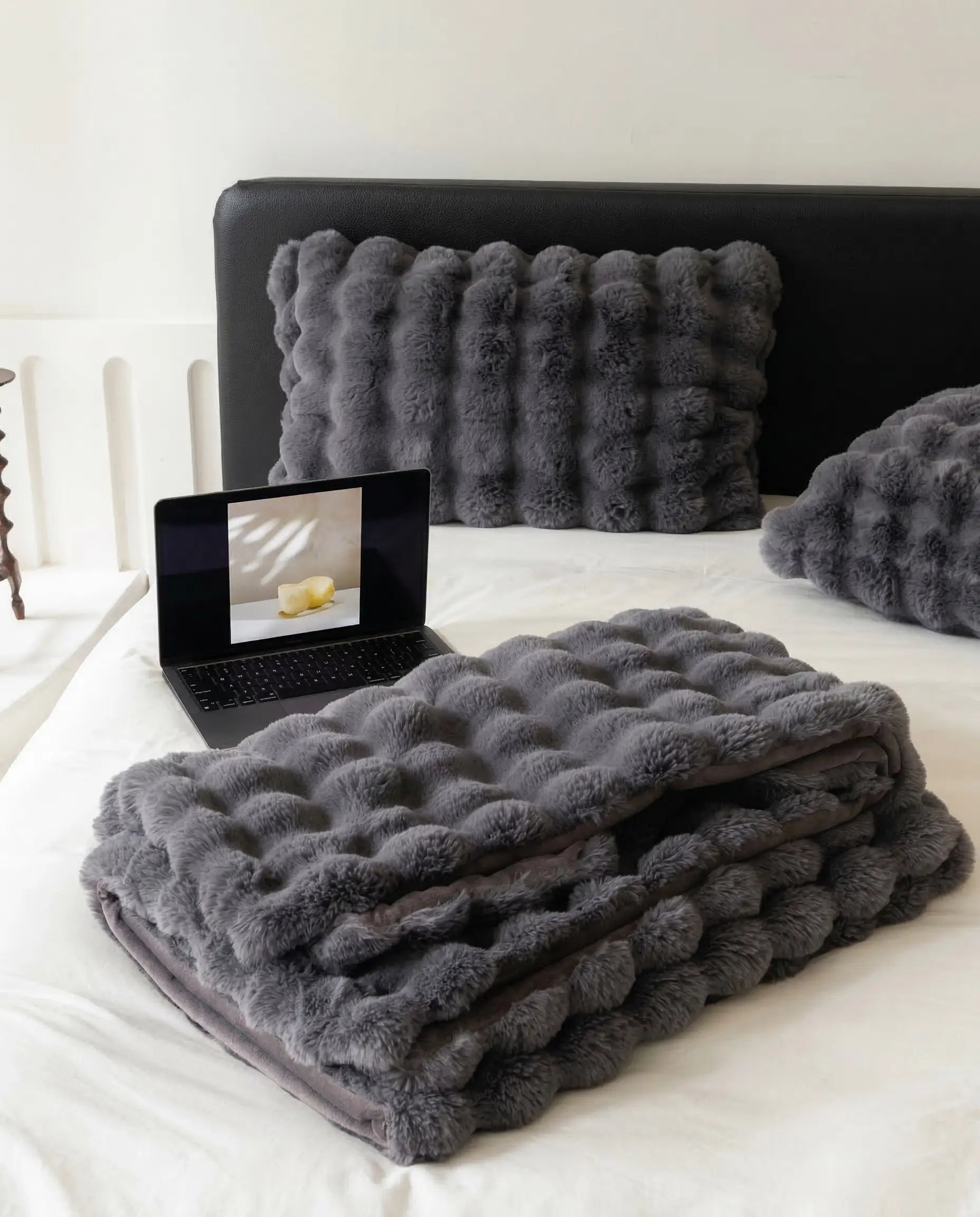 Folded DORMÉ Studio Marshmallow Ultra Plush Blanket in charcoal plush texture displayed on minimalist bed with matching pillows.