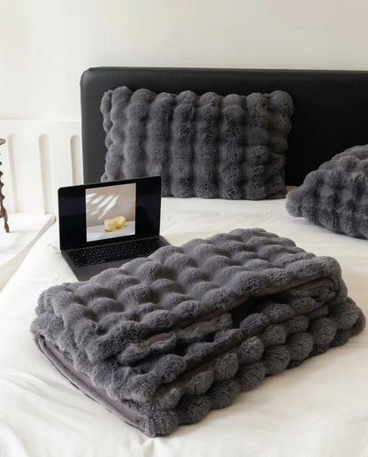 Folded DORMÉ Studio Marshmallow Ultra Plush Blanket in charcoal plush texture displayed on minimalist bed with matching pillows.