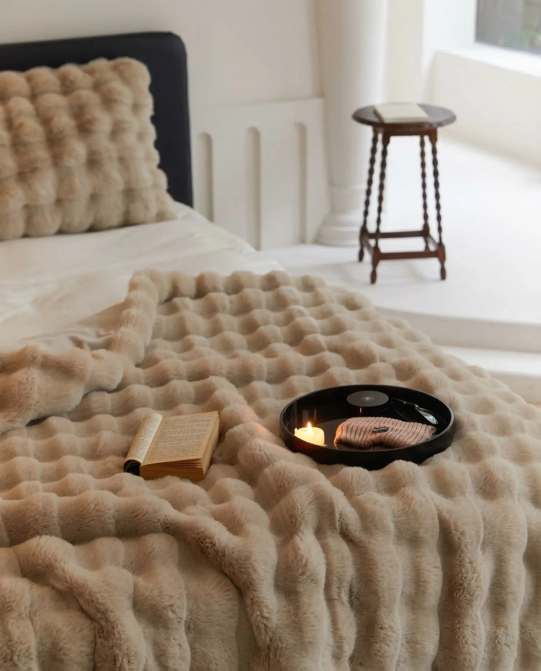 DORMÉ Studio Marshmallow Ultra Plush Blanket in khaki plush fabric styled on bed with book and candle creating cozy bedroom aesthetic.