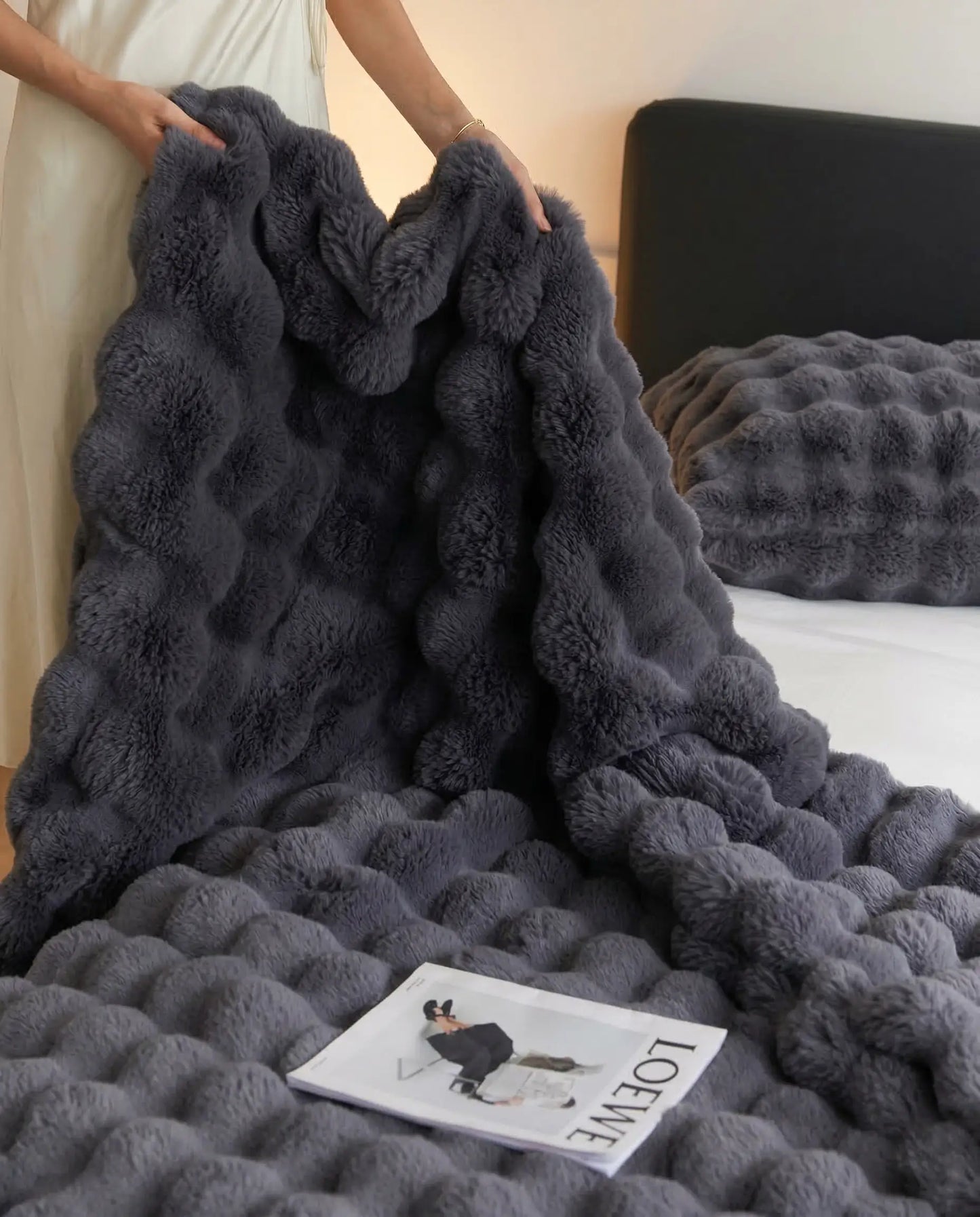Person lifting DORMÉ Studio Marshmallow Ultra Plush Blanket in charcoal plush fabric showing thick sculpted texture.