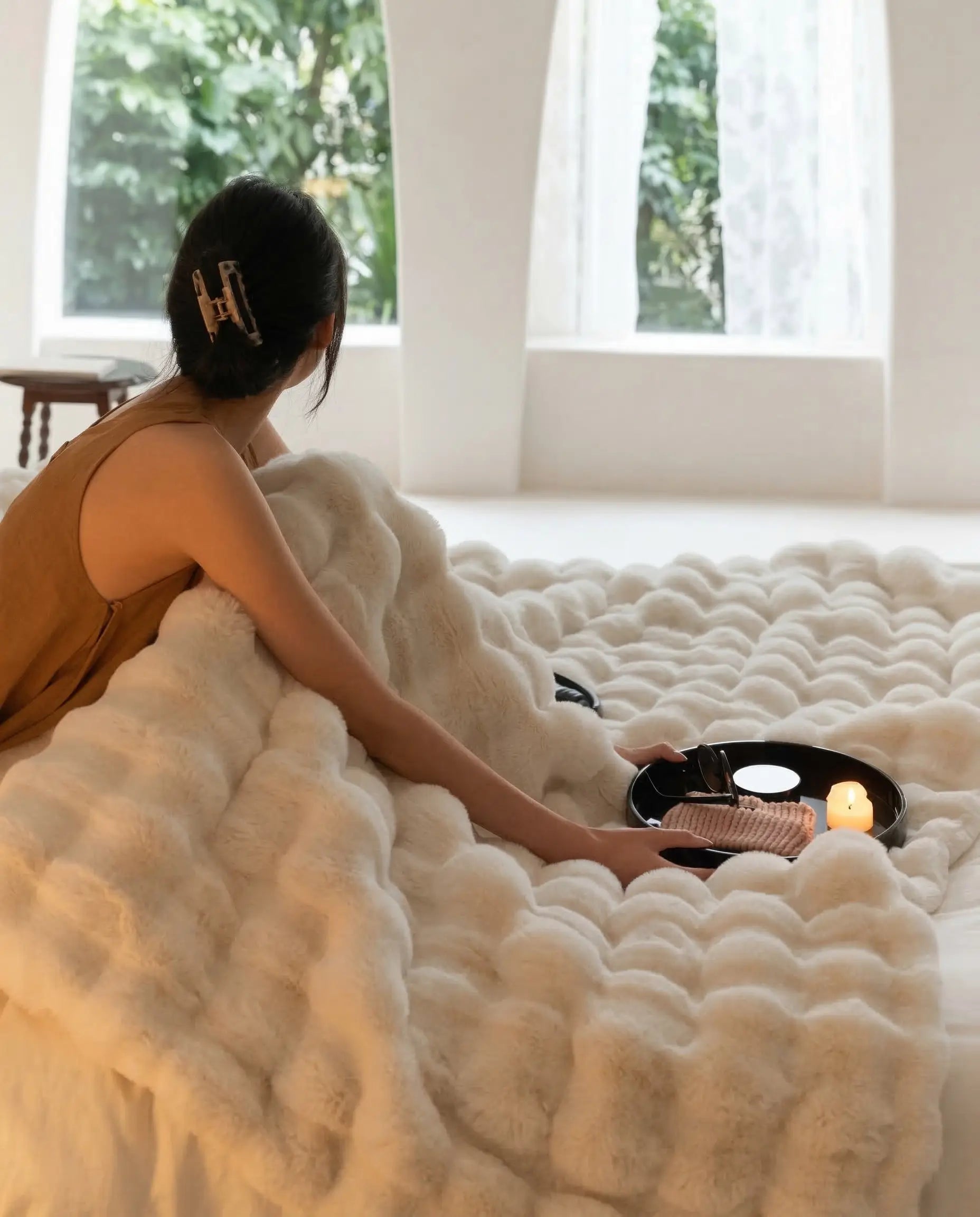 DORMÉ Studio Marshmallow Ultra Plush Blanket styled across bed with candle tray and magazine for luxury bedroom aesthetic.