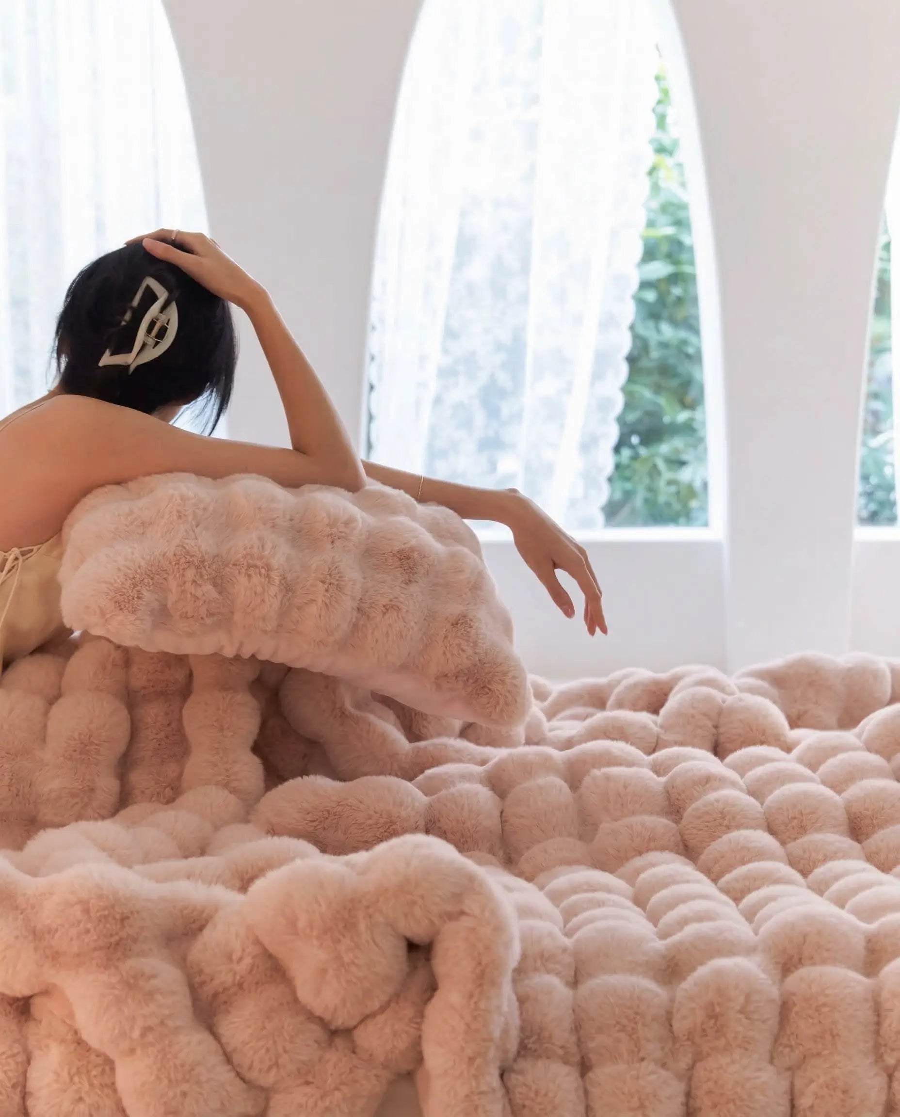 Woman resting on DORMÉ Studio Marshmallow Ultra Plush Blanket in pink plush texture creating a cozy luxury bedroom aesthetic.